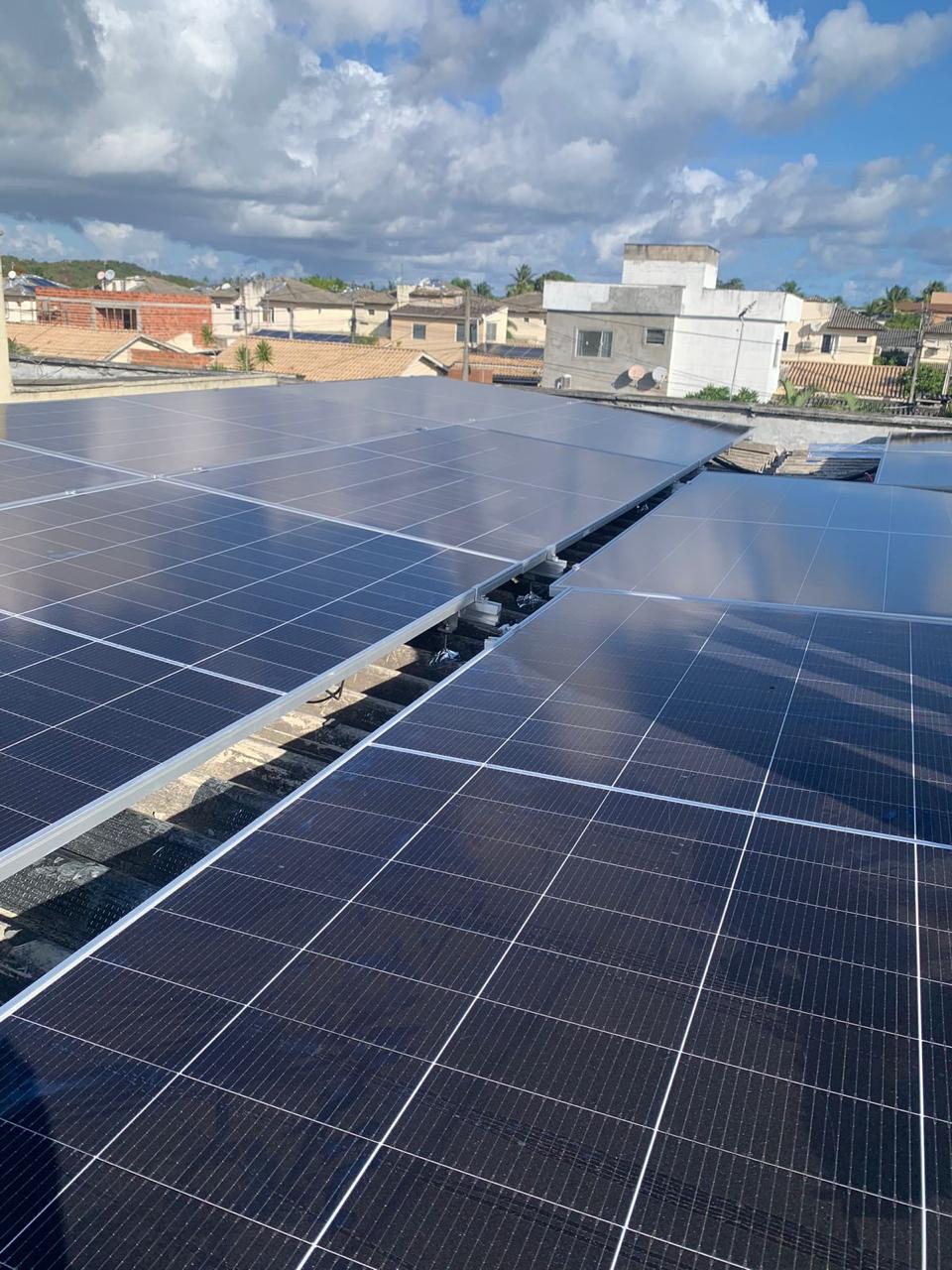 Painéis solares instalados no telhado de uma residência, com casas ao fundo.